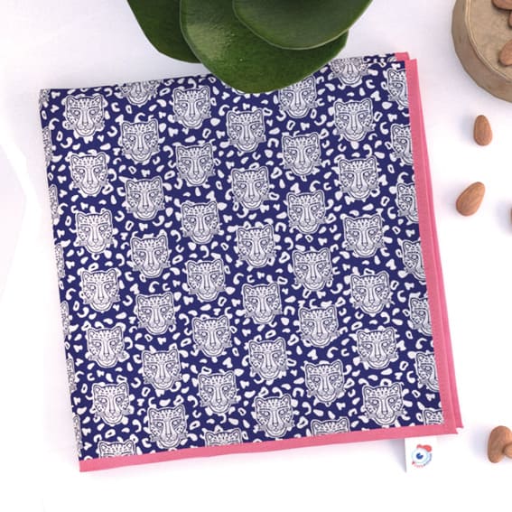 Ambiance serviette de table La Grrrminette Bleue bord rose de la famille GRRR. Têtes de léopard, fond bleu foncé, léopard et rosette blanche. Plante et amandes.