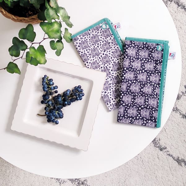 Lot de 2 serviettes de table en tissu, famille déco Grrr, motif léopard fond naturel et motif léopard fond bleu foncé. Ambiance grappe de raisin. Bord Turquoise
